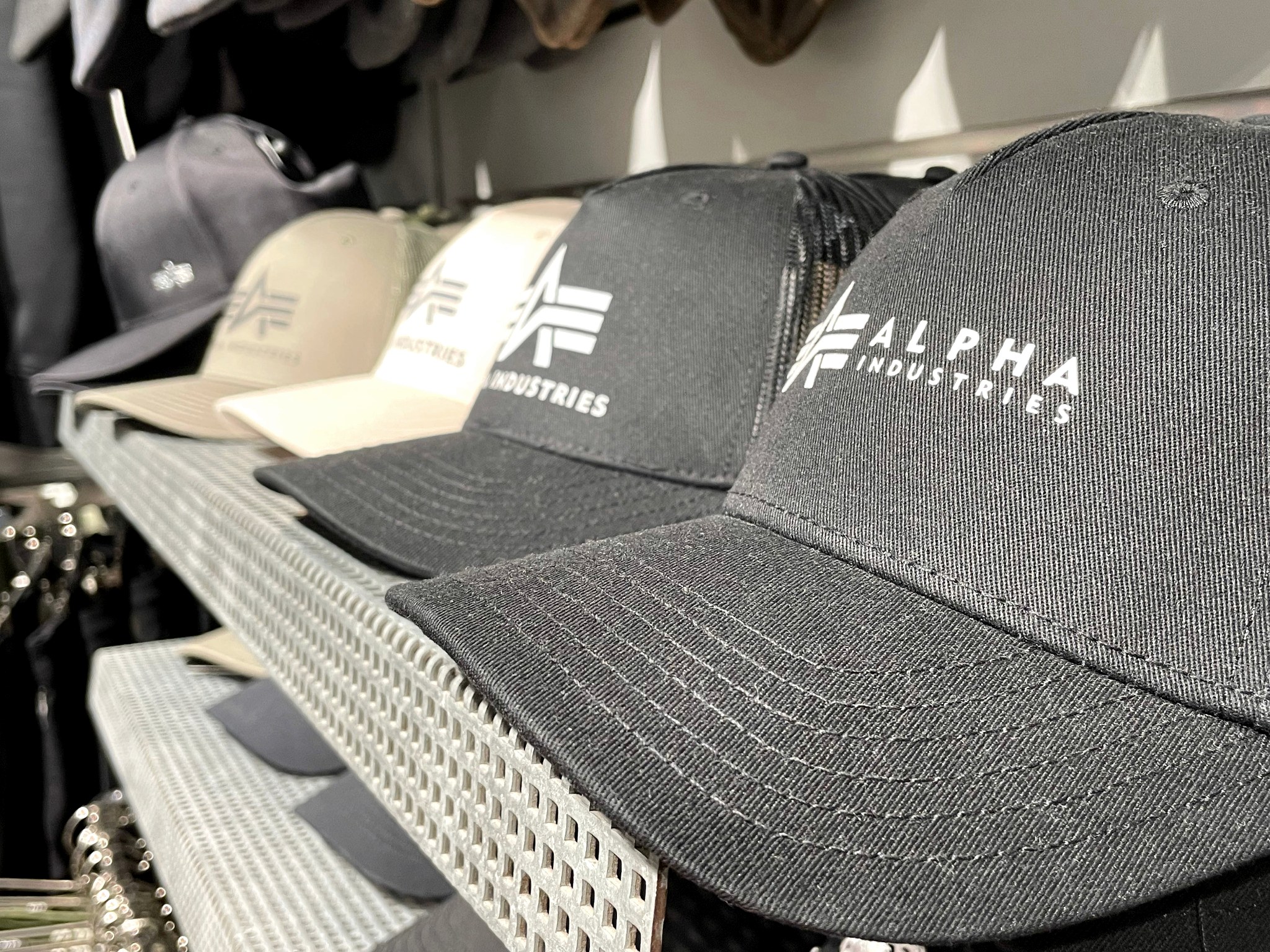 Reihe von Alpha-Industries-Caps in Schwarz, Grau und Sand im Regal des US SHOP Karlsruhe